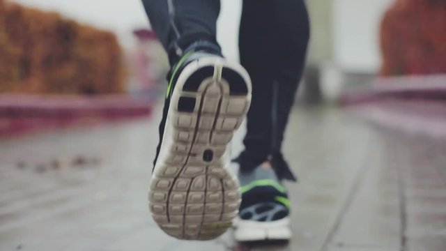 Man running on a wet concrete road. Close up tracking shot of legs of unidentified person jogging. Sport, healthy lifestyle concept.