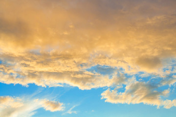 Golden fluffy clouds illuminated by the sunset against a blue sky (background)