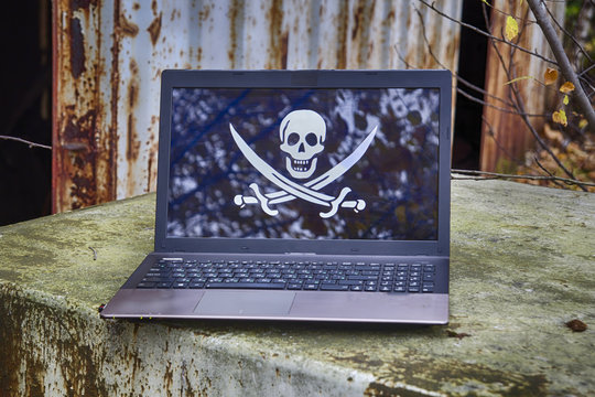 Laptop with a picture of a pirate flag "Jolly Roger" on the screen with rusty industrial destructed stuff on background