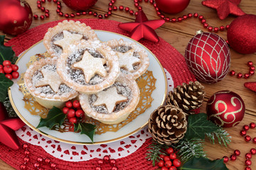 Christmas star mince pies with icing sugar dusting on a plate with bauble decorations, holly, ivy,...