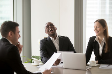 African american man laughing during successful negotiations with caucasian partners. Job applicant made pleasant first impression on recruiters with joke at interview. Good relationship in office