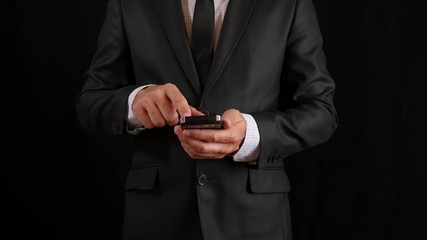 The concept, digital online life and social networks. A businessman in a black business suit with a tie uses his smartphone for business correspondence - 1