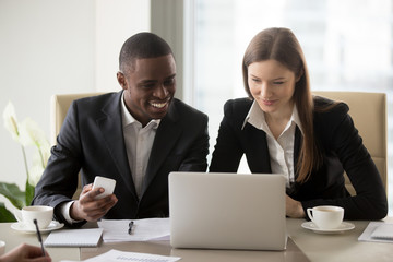 Satisfied multinational businesspeople sitting at work desk in front of laptop analyzing deal...