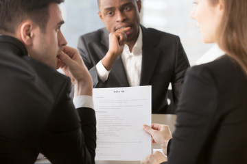 Back view of thoughtful HR managers reading, discussing candidates resume, worried african american job applicant waiting decision at interview on background. Anxiety, Lie, mistakes in questionable CV