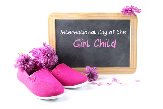 pink kid shoes and flowers in front of a writing blackboard with text International Day of the Girl Child,  isolated on a white background, date concept 11 October