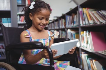 Girl on wheelchair using digital tablet in library