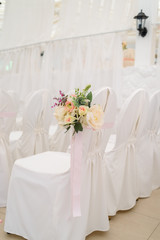 Fototapeta na wymiar Beautiful flower arrangement on white wedding chairs on each side of archway, selective focus. Empty chairs with white cloth for guests on wedding ceremony, free space
