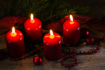Four red burning candles at the fourth advent, christmas decoration with spruce twigs and baubles on a rustic wooden table