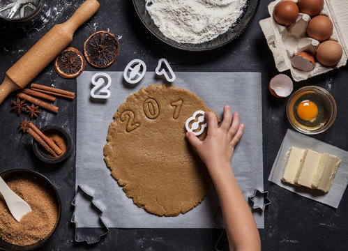 Child preparing Christmas bakery, cookies in shape 2018. Raw dough for holiday sweets. Home family cooking concept. Bakery ingredients, eggs, flour, butter, dried oranges and cinnamon.