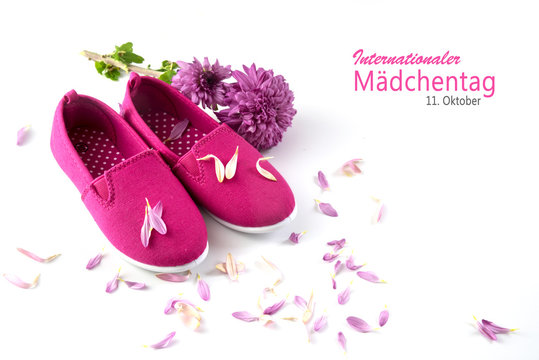 pink kid shoes, a flower and petals isolated on a white background, german text Internationaler Maedchentag, that means  International Day of the Girl Child, concept date 11 Octobe
