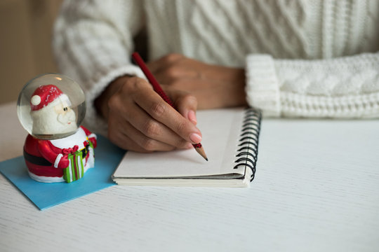 Hands with a pencil, notebook and an envelop for letter. A girl is ready to send a letter with wishes to Santa Claus. Christmas mood is to write letter or to draw a picture to make dreams come true.