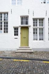 Green door on a white brick house with sash windows and straight metal anchor plates. Three steps lead up to the porch. House is close to the cobbled street. Little house in Antwerp Belgium.