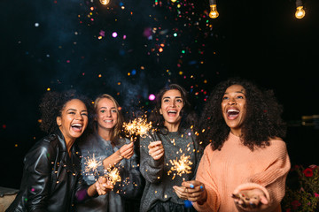Female friends having party at night outdoors, throwing confetti - obrazy, fototapety, plakaty
