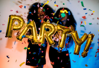 Two unrecognizable women holding party balloon under confetti.