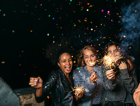 Group of happy friends celebrating new year's eve with confetti and sparklers