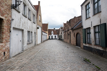 Fototapeta na wymiar Quaint little cobblestone street lined with small traditional brick houses in Bruges Belgium. Vernacular housing and cobbled road in Belgium. Quaint European street, no people.