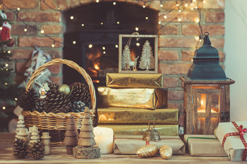 Dark Christmas composition, lantern, presents and handmade wooden decorations on the table in front of fireplace with woodburner, ornaments and garlands on the back, lights, selective focus, toned