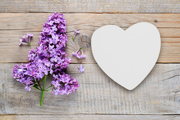 Lilac flowers and white heart on old wooden background
