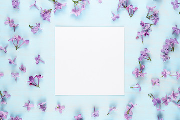 Blank greeting card and lilac flowers on blue background