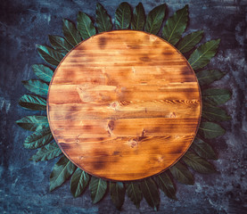 Round empty wooden cutting board with bay leaf around on a dark gray textured background. Top view. Copy space