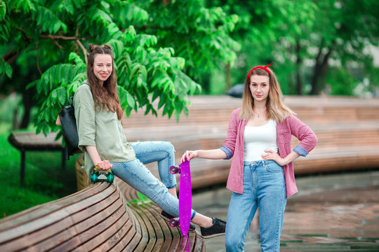 Two hipster girls with skateboard outdoors in the park. Active sporty women having fun together in skate park.