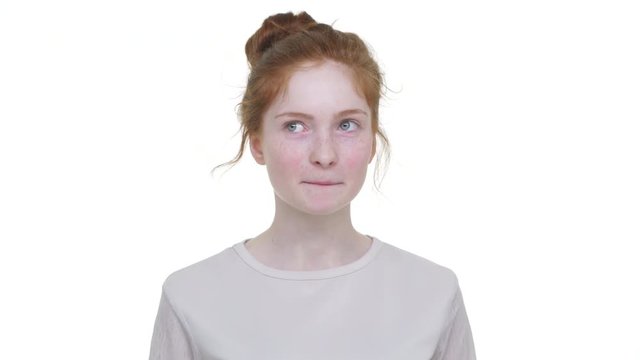 caucasian thoughtful young woman with tied ginger hair in topknot looking from side to side biting her lips over white background. Concept of emotions