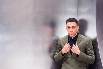Portrait of young American Businessman in New York, wearing green suit, black undershirt, hands on lapels, standing by sliver metal wall, looking at you, thinking. Color filtered with purple tint..