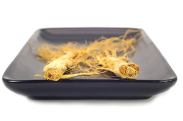 Ginseng root on the black plate isolated in white background.