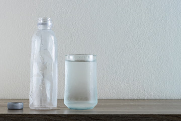 glass of water with plastic water bottle on wooden table.