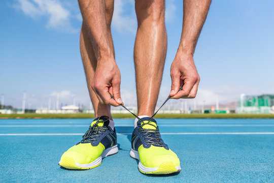 Runner tying running shoes laces on run tracks lanes in stadium getting ready for race competition outdoor on track and field. Sport athlete man jogging motivation.
