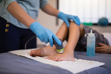 Female therapist wearing gloves scanning feet of boy lying on