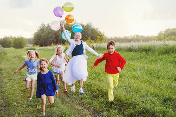 Fototapeta premium cheerful smiling elementary school age boy and girls holding air balloons and running in summer park. Selective focus