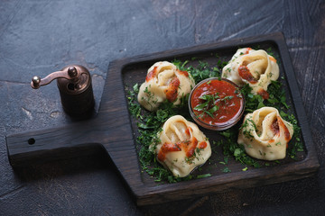 Steamed meat dumplings or manti with tkemali sauce and greens on a dark brown stone background, horizontal shot