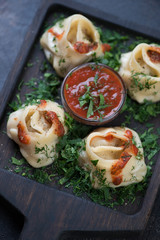 Closeup of manti or steamed meat dumplings on a black wooden serving tray, selective focus, elevated view