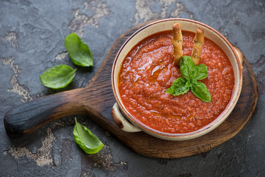Gazpacho soup with fresh green basil leaves on a brown stone background, studio shot