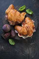 Croissants with prosciutto ham and ripe figs on a dark brown stone background, above view with space