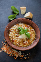 Soup with lentils and pasta served in a clay plate, vertical shot