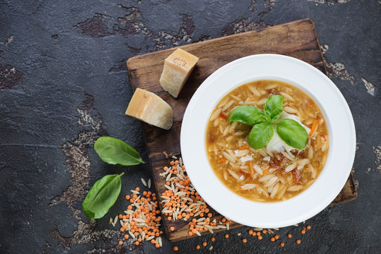Plate of lentil and pasta soup with addition of parmesan on a brown stone background, above view with space, horizontal shot