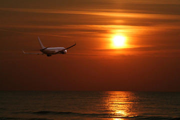 plane flying over the sea towards the setting sun