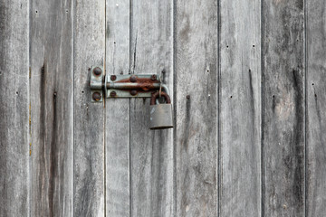 Detail of an old unpainted plank door secured with a rusty bolt and padlock.