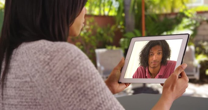 Over the shoulder shot of black woman video chatting male friend with tablet