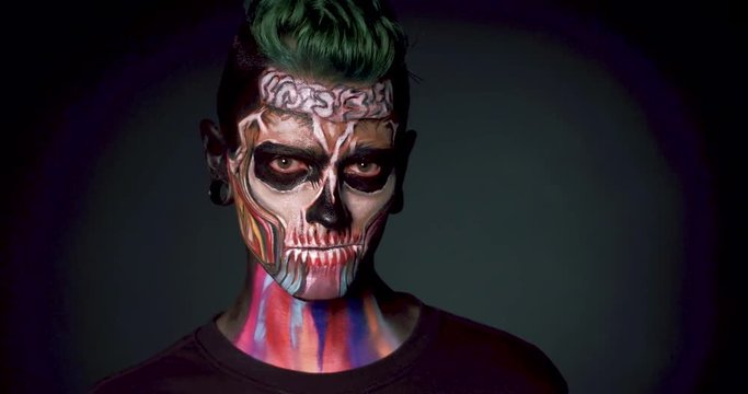 Death face colored makeup for Halloween. Zombie man looking at camera.