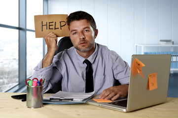 businessman suffering stress working at computer desk holding sign asking for help looking tired...