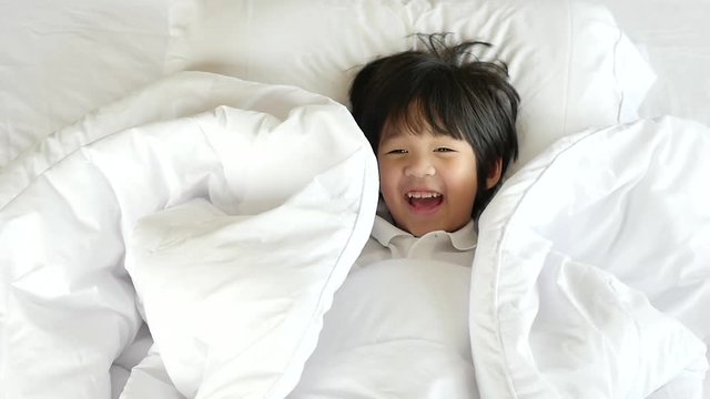 Cute asian child playing hide and seek on white bed slow motion 
