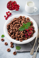 Healthy breakfast with chocolate corn rings, red currant berries, yogurt and tea on a gray concrete background. Selective focus. Top view. Copy space.