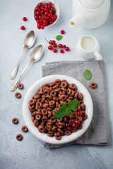Healthy breakfast with chocolate corn rings, red currant berries, yogurt and tea on a gray concrete background. Selective focus. Top view. Copy space.