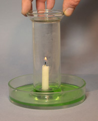 Lit candle stands in water (sligt colored for better visualisation). The candle uses the oxygen, and the water level rises up in the glass as the candle goes out due to lack of oxygen.