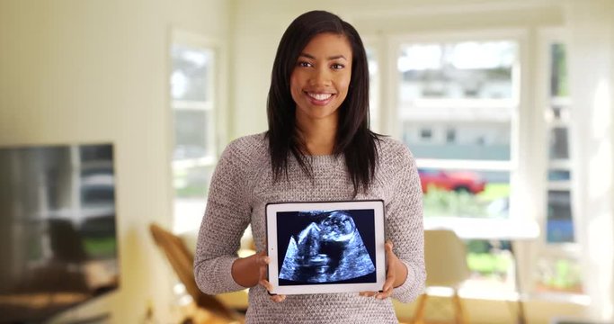 Portrait of joyful black female showing ultrasound picture on tablet 