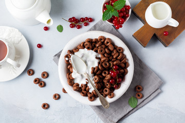 Healthy breakfast with chocolate corn rings, red currant berries, yogurt and tea on a gray concrete background. Selective focus. Top view. Copy space.