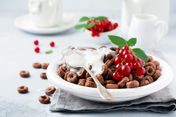 Healthy breakfast with chocolate corn rings, red currant berries, yogurt and tea on a gray concrete background. Selective focus. Copy space.
